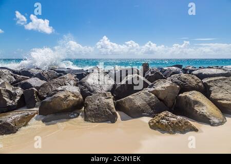 Sable et rochers sur une plage de la Barbade, avec des vagues qui s'écrasant sur les rochers Banque D'Images