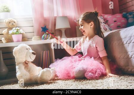 Une fille heureuse joue avec une baguette magique et un ours en peluche à la maison. Drôle, un enfant adorable s'amuse dans la chambre des enfants. Banque D'Images