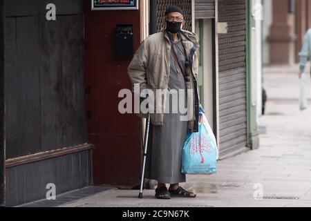 Un homme tenant un bâton de marche et portant un masque chirurgical noir se tient dans la rue à Cardiff, Royaume-Uni Banque D'Images