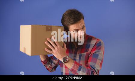 Jeune homme avec une boîte en carton dans sa main. Écouter pour voir ce qui a été livré. Photo de haute qualité Banque D'Images