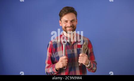 Un jeune homme, un réparateur ou un homme à main qui tient des outils. Isolé sur fond bleu. Photo de haute qualité Banque D'Images