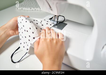 Femme couture mains d'un masque médical visage à une machine à coudre. Faites-le vous-même, zéro gaspillage et coronavirus concepts. Banque D'Images