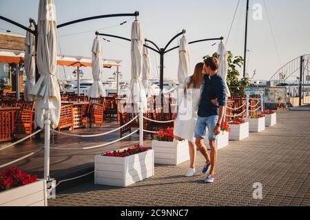 ODESSA, UKRAINE - 06 AOÛT 2015: Joli jeune beau couple embrassant à la jetée au port avec de petits yachts et café d'été, heureux sourire en plein air Banque D'Images