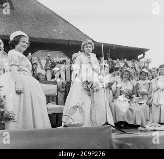 Années 1950, historique, sur une plate-forme à l'extérieur d'un pavillon sportif en bois à Farnworth, Lancashire, une jeune fille, faisant un discours à la cérémonie de la Reine de la Rose. D'autres enfants sont également vêtus de robes. La « Rose Reine » serait à la tête de la traditionnelle procession ou parade connue sous le nom de « Journée de marche », des célébrations qui étaient communes dans le nord-ouest de l'Angleterre, au Royaume-Uni dans cette époque. Un événement annuel, certains remontent aux années 1830 où ils étaient des défilés d'église liés aux écoles du dimanche des enfants et beaucoup sont encore aujourd'hui. Banque D'Images