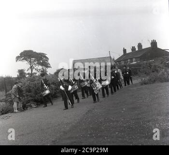 Années 1950, historique, sur un chemin dans un parc ou un terrain de sport à Farnworth, dans le Lancashire, un groupe de jeunes marchant prenant part à la traditionnelle Rose Queen parade. Dans une robe et portant un tiara, la « Reine de la Rose » allait mener la procession ou le défilé connu sous le nom de « Journée de marche », des célébrations qui étaient communes dans le nord-ouest de l'Angleterre, au Royaume-Uni dans cette époque. Un événement annuel, certains remontent aux années 1830 où ils étaient des défilés d'église liés aux écoles du dimanche des enfants et beaucoup sont encore aujourd'hui. Banque D'Images