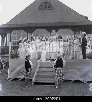 Années 1950, historique, sur une plate-forme à l'extérieur d'un pavillon de sport en bois à Farnworth, Lancashire, une adolescente, la « Rose Reine » récemment couronnée de la ville, fait un discours. D'autres enfants sont en costumes et les petits garçons portent des fours à tartan. Dans une robe et portant un tiara, la « Reine de la Rose » serait à la tête de la traditionnelle procession ou parade connue sous le nom de « Journée de marche », des célébrations qui étaient communes dans le nord-ouest de l'Angleterre, au Royaume-Uni dans cette époque. Un événement annuel, certains remontent aux années 1830 où ils étaient des défilés d'église liés aux écoles du dimanche des enfants et beaucoup sont encore aujourd'hui. Banque D'Images