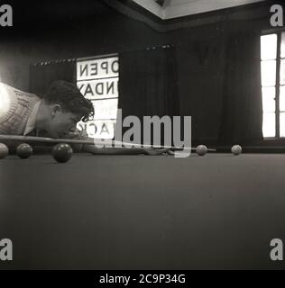 Années 1950, historique, un jeune homme jouant au snooker dans une cabane dans un camp de vacances britannique, Angleterre, Royaume-Uni. En cette époque, les camps de vacances en bord de mer étaient très populaires en Grande-Bretagne et avaient de nombreuses installations de loisirs pour les clients, y compris des foires de funkers, des piscines, un vert d'exercice et une piscine/snooker. Banque D'Images