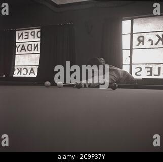 Années 1950, historique, un jeune homme jouant au snooker dans une cabane dans un camp de vacances britannique, Angleterre, Royaume-Uni. En cette époque, les camps de vacances en bord de mer étaient très populaires en Grande-Bretagne et avaient de nombreuses installations de loisirs pour les clients, y compris des foires de funkers, des piscines, un vert d'exercice et une piscine/snooker. Banque D'Images