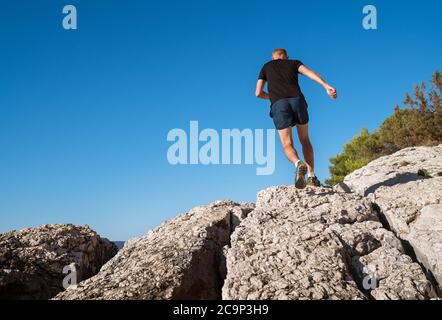 Active montagne Skyrunner habillé t-shirt noir et chaussures de course jogging le sommet de la falaise pendant le scamper matin. Les sportifs s'y mènent dans un grand nombre d'activités Banque D'Images