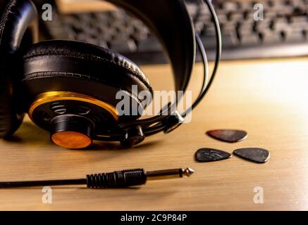 Un casque et une guitare se piquent avec un clavier d'ordinateur à l'arrière-plan sur un bureau en bois Banque D'Images