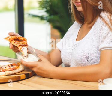 Une fille trempe une tranche de pizza dans une sauce dans un récipient en plastique avant de la manger Banque D'Images