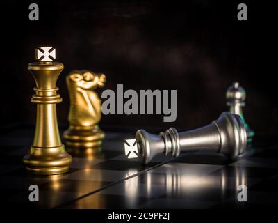 Le roi d'or d'échecs est entouré de tomber autour des pièces d'échecs d'argent à la lutte avec le travail d'équipe à la victoire, le concept de stratégie d'affaires et de leader et Banque D'Images