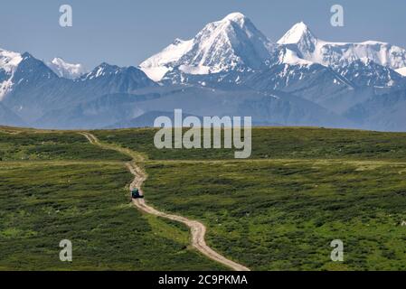 Vue incroyable avec une voiture sur une route sinueuse en terre qui longe la pente de la montagne parmi les épaissis des buissons nains de bouleau sur le fond o Banque D'Images