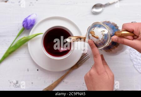 La femme verse du thé rouge chaud dans une tasse sur une table en bois blanc Banque D'Images