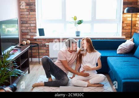 homme beau et prudent avc ventre de femme enceinte, couple marié passer le week-end à la maison, se reposer. homme et femme en tenue domestique, pyjama Banque D'Images