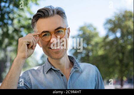 Portrait d'un homme d'affaires mûr élégant portant des lunettes, debout dans la rue, regardant l'appareil photo, souriant Banque D'Images