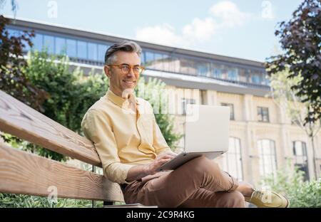 Confiant auteur indépendant utilisant ordinateur portable, dactylographiant sur le clavier, regardant la caméra, souriant Banque D'Images