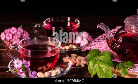 Les feuilles de thé vert ou les feuilles d'herbes médicinales sont sur la table avec une théière et des tasses de thé rouge, de noix de cajou et de fleurs de clou de girofle. Fêtes de thé, trad de thé Banque D'Images