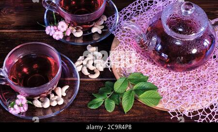 Les feuilles de thé vert ou les feuilles d'herbes médicinales sont sur la table avec une théière et des tasses de thé rouge, de noix de cajou et de fleurs de clou de girofle. Fêtes de thé, trad de thé Banque D'Images