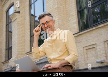 Portrait d'un beau projet d'homme mature, assis à l'extérieur. Auteur indépendant confiant utilisant ordinateur portable, regardant la caméra Banque D'Images