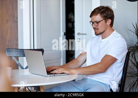 vue latérale sur un homme qui travaille avec un ordinateur portable, un homme confiant dans des lunettes se concentre sur le travail, tapant sur le clavier Banque D'Images