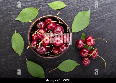 Cerise douce mûre dans une assiette noire sur fond de pierre sombre. Baies fraîches d'été pour une alimentation saine. Vue de dessus, espace de copie. Banque D'Images