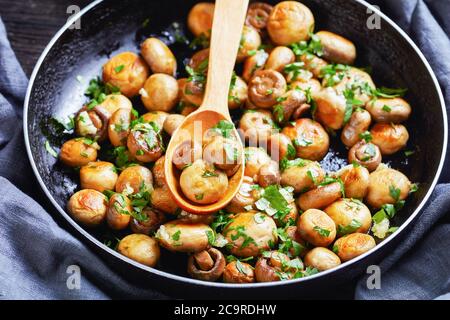 Faire sauter dans de l'huile d'olive de petits champignons d'ail avec du persil haché et du jus de citron appelé al ajillo en Espagne servi sur une poêle sur un b en bois sombre Banque D'Images