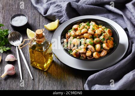 Tapas aux champignons de l'ail espagnol al ajillo ail rôti champignon champignons avec persil haché, ail, jus de citron sur une assiette noire sur table en bois Banque D'Images