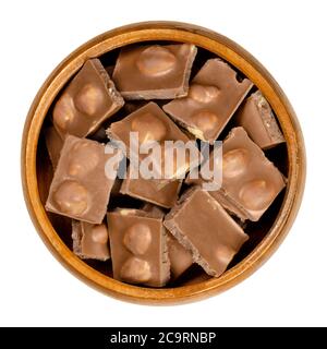 Chocolat au lait de noisette, barres cassées en morceaux, dans un bol en bois. Petits segments de la barre de bonbons. Chocolat au lait avec noisettes grillées entières. Banque D'Images