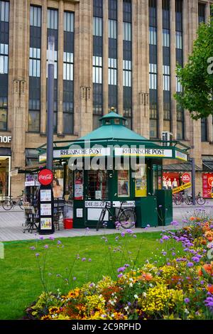 Kiosque à journaux en face du grand magasin Kaufhof à Königsallee à Düsseldorf lors d'une belle journée d'été avec fleurs d'été et prairie verte. Banque D'Images