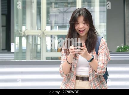 La jeune fille chinoise réagit avec joie en souriant heureusement après avoir lu de bonnes nouvelles sur son téléphone portable. Banque D'Images