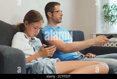 Une famille ordinaire moderne. Papa regarde la télévision, la fille joue sur le smartphone. Banque D'Images