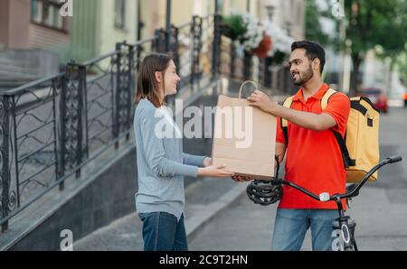 Faire du shopping à la maison. Messagerie amicale avec sac à dos et vélo donne le sac en papier au client Banque D'Images