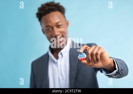 Homme afro-américain montrant une épingle de vote, arrière-plan flou Banque D'Images