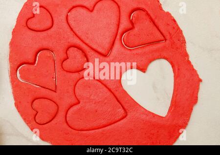 Pâte rouge avec un cœur sculpté de différentes tailles sur une table blanche. Vue de dessus, gros plan Banque D'Images