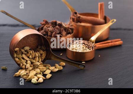 Concept alimentaire mélange d'épices de masala, cannelle, fenouil, anis étoilé, graines de coriandre et gousses de cannelle dans une tasse de cuivre sur un panneau d'ardoise noir Banque D'Images