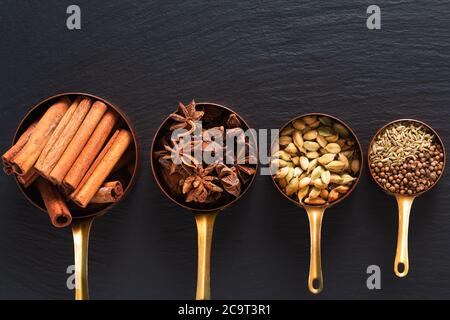 Concept alimentaire mélange d'épices de masala, cannelle, fenouil, anis étoilé, graines de coriandre et gousses de cannelle dans une tasse de cuivre sur un panneau d'ardoise noir Banque D'Images