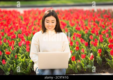 Femme asiatique utilisant un ordinateur portable, assise sur un parapet Banque D'Images