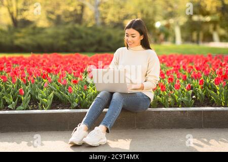 Fille asiatique utilisant un ordinateur portable, assis sur un parapet dans le parc Banque D'Images