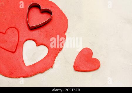 Pâte rouge avec une forme pour couper et couper les coeurs sur une table blanche, espace pour le texte, gros plan Banque D'Images