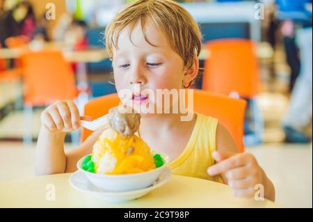 Charmant petit garçon blond qui mange de la glace dans le café de la ville en été Banque D'Images