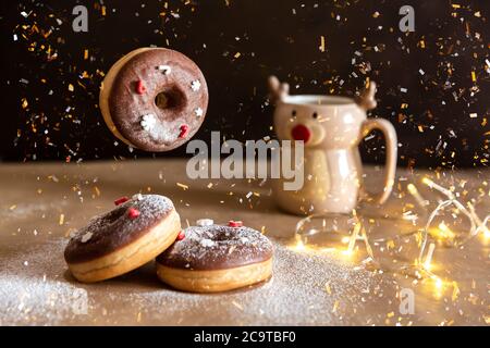 Table de petit-déjeuner de Noël avec beignet de chocolat volant décorée de saupoudrés rouges et blancs, chocolat chaud dans une tasse de cerf sur fond Banque D'Images