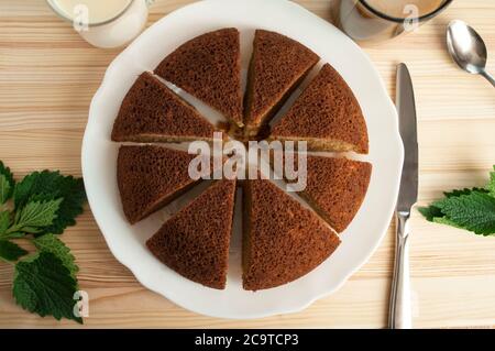 Tranché, divisé tarte éponge en sable portionsand et une tasse de café avec du lait sur un fond en bois. Pose à plat. Minimaliste. Banque D'Images