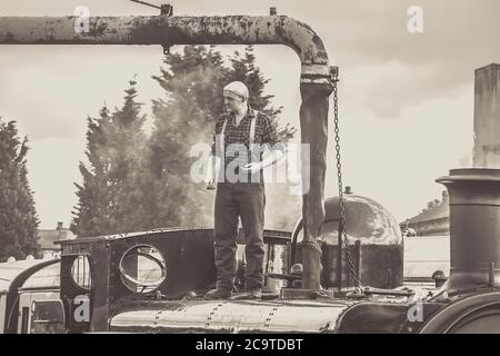 Équipe de moteur monochrome pompier remplissant le réservoir d'eau de la locomotive à vapeur d'époque 7714, Severn Valley Heritage Steam Railway, Kidderminster, Royaume-Uni. Banque D'Images