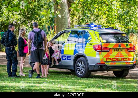 Londres, Royaume-Uni. 02 août 2020. Une unité de police armée fait un arrêt de bonne volonté après que des enfants se soient défertés à leur passage dans le parc St James. Ils s'arrêtent, les laissent grimper dans la voiture et leur donnent des autocollants. Dans ce monde covid19, ils manquent cependant des masques et de la distance sociale, mais il est possible que le père soit un collègue. Crédit : Guy Bell/Alay Live News Banque D'Images