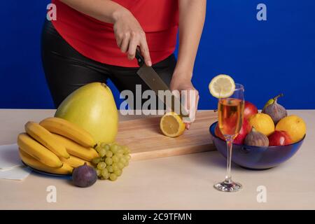 Femme en blouse rouge tranches de citron sur un bois montez sur une table avec un grand couteau de cuisson un arrière-plan bleu Banque D'Images