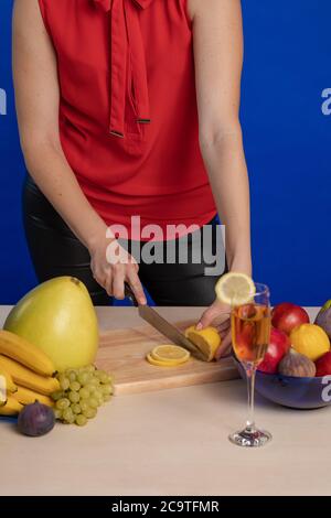 Femme en blouse rouge tranches de citron sur un bois montez sur une table avec un grand couteau de cuisson un arrière-plan bleu Banque D'Images