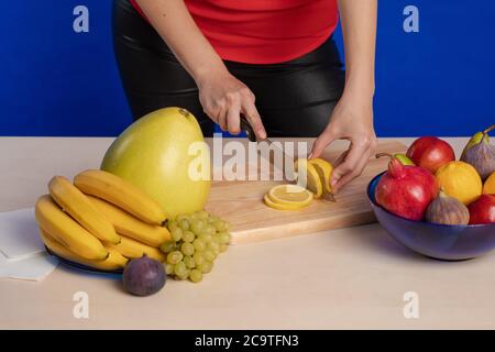Femme en blouse rouge tranches de citron sur un bois montez sur une table avec un grand couteau de cuisson un arrière-plan bleu Banque D'Images