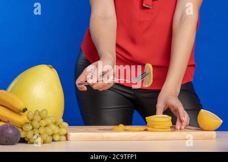 Femme en blouse rouge tranches de citron sur un bois montez sur une table avec un grand couteau de cuisson un arrière-plan bleu Banque D'Images