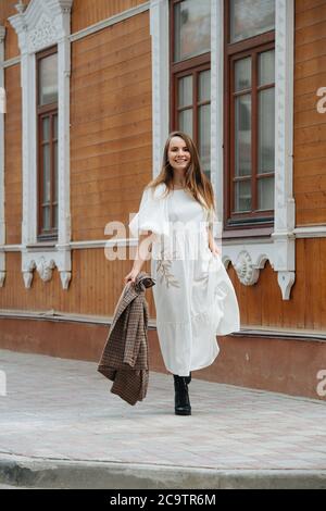 Une jeune femme heureuse marchant dans la rue dans une robe blanche moelleuse Banque D'Images